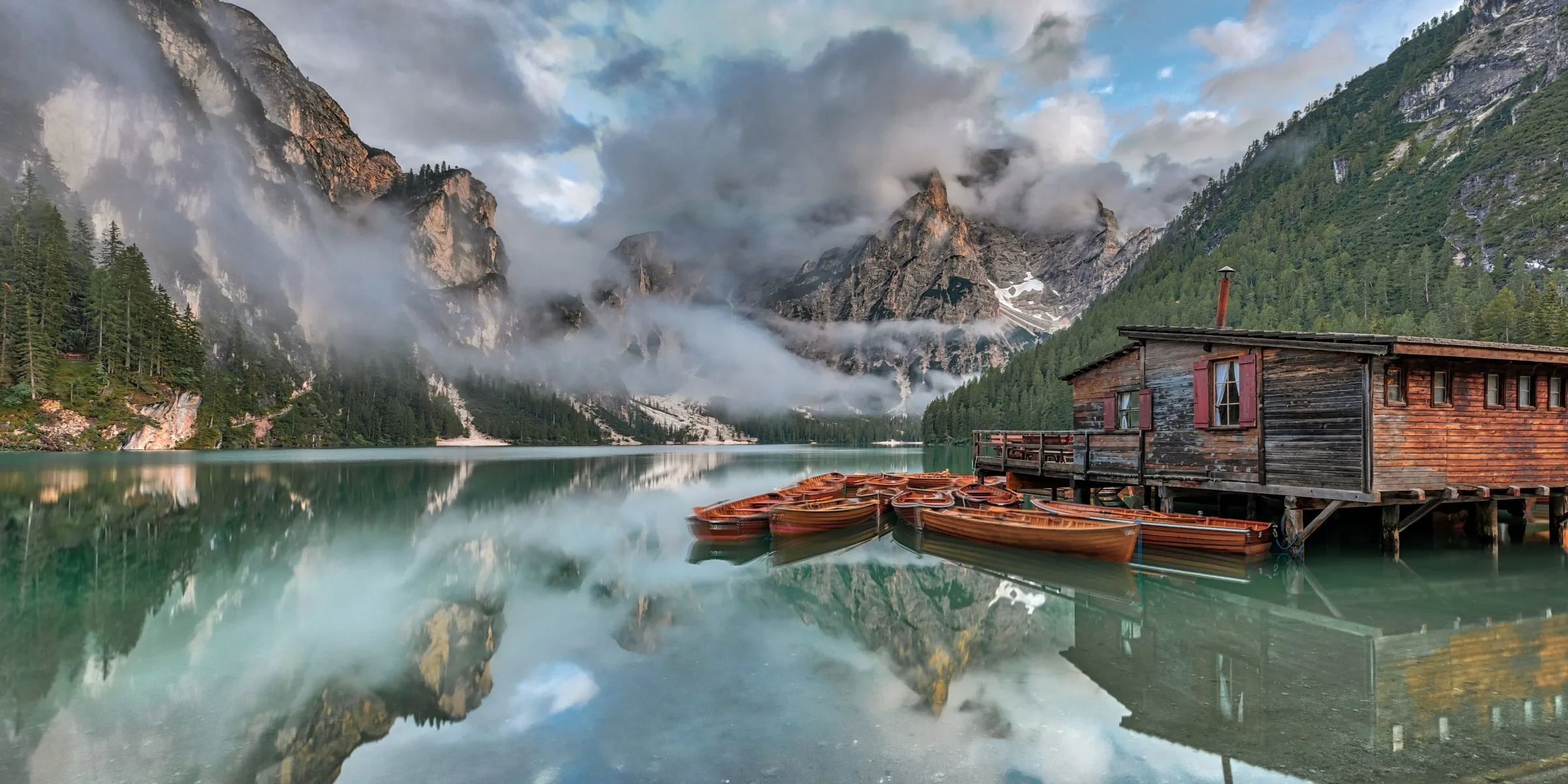 Still turquoise lake beneath pale mountain peaks at first light.