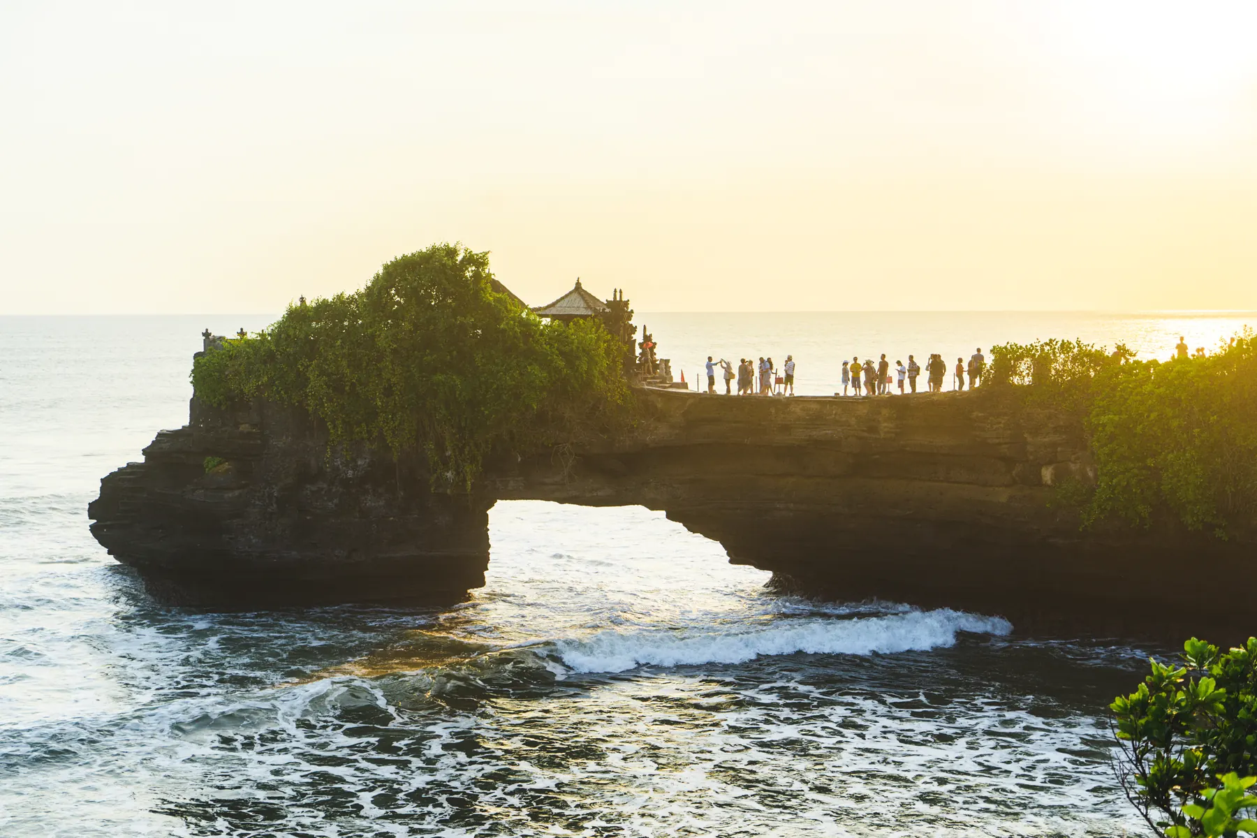 The sea temple of Tanah Lot in Bali on its rock arch, surf breaking below at sunset.